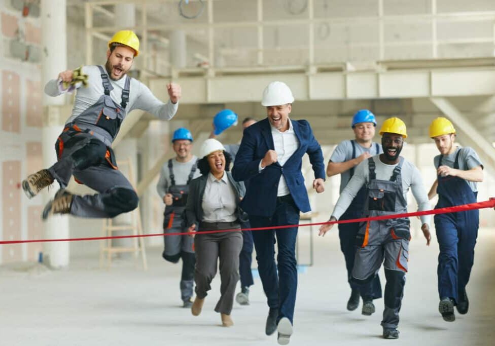 Cheerful manual worker and project manager having fun while crossing the finish line before their colleagues at construction site.