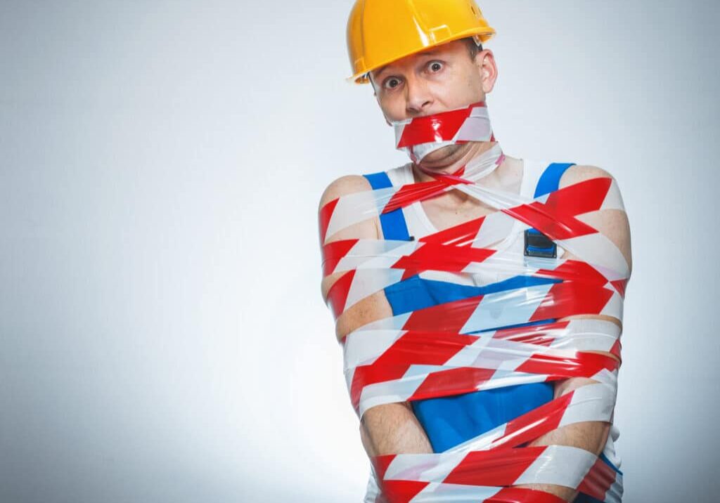Funny builder wrapped with coution tape. Isolated on gray.