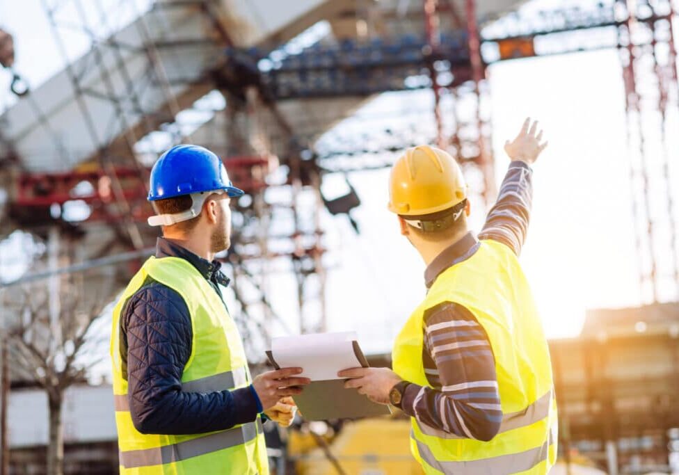 Two experts engineers in protective helmets and fluorescent vests showing the construction site and building activities after the successful project phase. Image taken with Nikon D800 and 85mm developed from RAW in XXXL size, in Novi Sad, Serbia, Central Europe, Europe