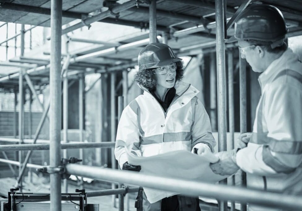 a female construction agent discusses progress with a male contractor or architect on a housing development construction site.